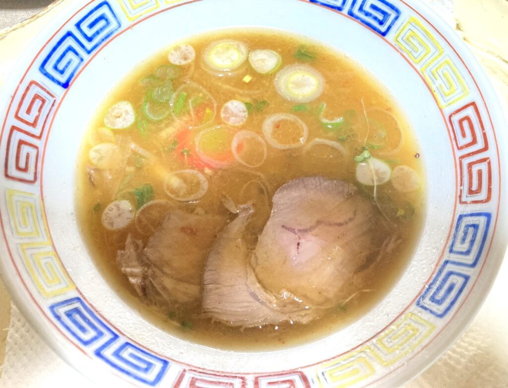 チャーシュー3枚トッピング。ネギを散りばめたつけ麺スープが器に入っている画像。