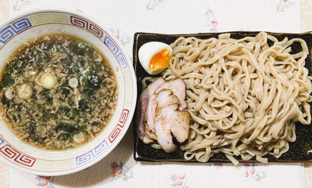 ネギとほうれん草と背脂が見えるつけ麺タレ&つけ麺の画像(つけ麺側には茹で卵とチャーシュートッピングあり)